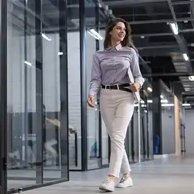 Una mujer vestida de forma semiformal camina hacia un edificio de gobierno con una carpeta en mano, para mostrar informe realizado con conocimientos obtenidos en una especialización en gestión pública.